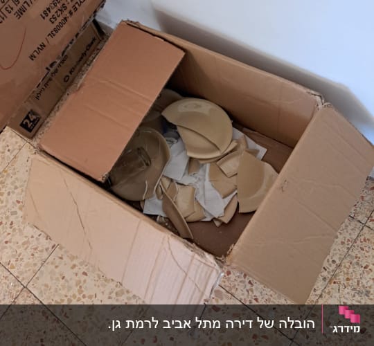 קרטון פתוח עם כלים שבורים על רצפה